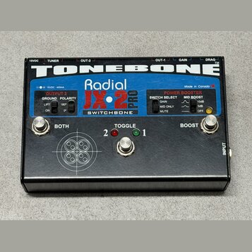 Černý efekt pedál s nápisy TONEBONE, Radial JX-2 PRO a SWITCHBONE. Na horní straně jsou ovládací prvky: dva stisknuté přepínače s popisky BOTH a BOOS…