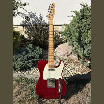 Elektrická kytara typu Telecaster v červené barvě s bílým pickguardem a světle hnědým javorovým hmatníkem. Na hlavě je viditelné logo Fender. Povrch…