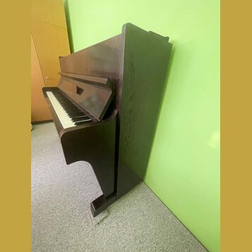 Tmavně hnědé digitální piano s dřevěnou texturou povrchu. Nástroj má klasický tvar s klaviaturou a integrovaným stojanem. Na viditelných částech nejs…