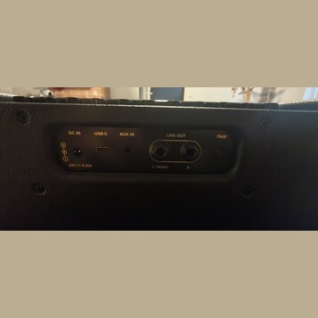 Detail zadního panelu černého hudebního zařízení s konektory. Jsou zde viditelné nápisy DC IN, USB-C, AUX IN, LINE OUT (s označením L / MONO a R) a P…