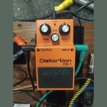Oranžový efekt pedál s černým spínacím tlačítkem. Na zařízení jsou nápisy Distortion, DS-1 a logo BOSS. Pedál má tři stříbrné oválné knoflíky s popis…