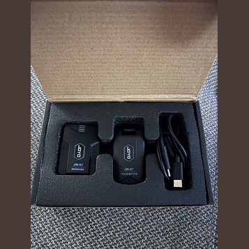 V kartonové krabici s pěnovým vložkem jsou dvě černé bezdrátové jednotky a černý USB kabel. Na levé jednotce je nápis JOYO, JW-07 RECEIVER a na pravé…
