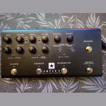 Černý kytarový zesilovač s nápisem AMPED 3 a doplňujícím textem DEPT. 10 | 100W 3 CHANNEL AMP. Na horním panelu se nachází dvanáct ovládacích knoflík…