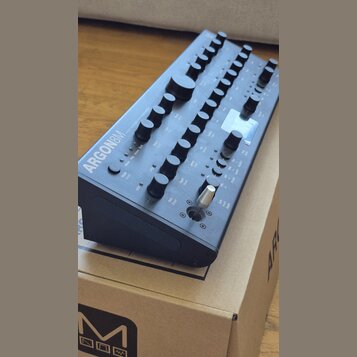 Černý syntetizátor s nápisem ARGON8M a doplňkovým textem POLYPHONIC TABLE WAVE SYNTHESIZER MODULE. Přístroj má kovové tělo s mnoha ovládacími knoflík…
