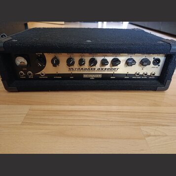 Černý basový zesilovač s kovovým předním panelem. Na panelu je nápis BEHRINGER a model ULTRABASS BX3000T s doplňujícím textem 300-WATT BASS AMPLIFIER…