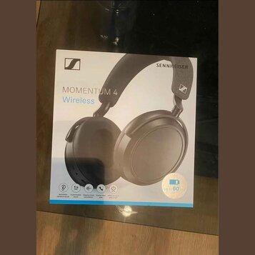 Fotografie znázorňuje krabici s černými bezdrátovými sluchatky. Na obalu je uveden nápis SENNHEISER, logo značky a model MOMENTUM 4 Wireless. V dolní…