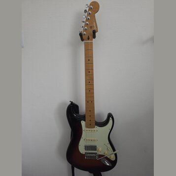 Elektrická kytara s tmele s gradací barvy od černé k hnědé a krčkem ze světlého dřeva. Na hlavě je viditelné logo Fender. Kytara má bílý pickguard, t…