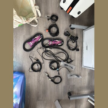 Fotografie zobrazuje sadu různých audio kabelů rozložených na šedé podlaze. Jsou zde černé kabely s různými konektory, včetně dvou kabelů v fialových…