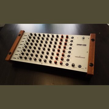 Stříbrný analogový drum synthesizer s dřevěnými bočními panely. Na pravé straně je uveden název modelu DRM1 MK III a značka VERMONA. Přístroj obsahuj…