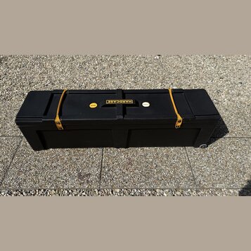 Černý plastový přepravní kufr s koly. Na horní části je umístěno logo HARDCASE a malý žlutý štítek s nečitelným nápisem. Kufr je zajištěn dvěma žlutý…