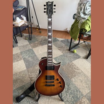 Elektrická kytara s trupem v hnědém sunburst provedení a viditnou strukturou dřeva. Na hlavě je bílé logo LTD a nápis Deluxe, na hmatníku jsou bílé v…