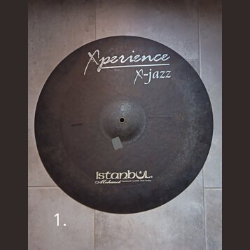 Kulatý činel s tmavým, matným povrchem. Na horní části je bílý nápis „Xperience“ a pod ním „X-jazz“, vlevo od něj je menší nečitelný text. Ve spodní…