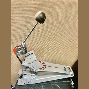 Stříbrný bubnový pedál s logem Pearl na základně a na beateru. Na pedálu je připevněna bílá visačka s nápisy DRUM PEDAL a MODEL NO. P-930. Povrch ped…