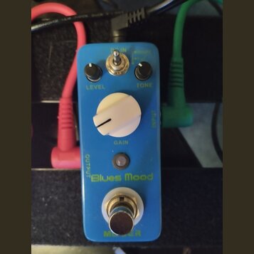 Modrý kytarový efekt s nápisem Blues Mood. Na horní části jsou dva černé otočné knoflíky s popisky LEVEL a TONE, přepínač a velký bílý knoflík s popi…