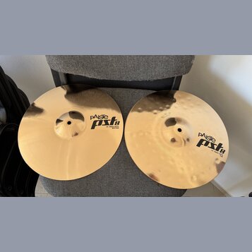 Dvě mosazné činely položené na šedém textilním povrchu. Horní činel má hladký povrch a nápis PAiste PSL 8 14" HI-HAT BOTTOM. Dolní činel má kovaný po…
