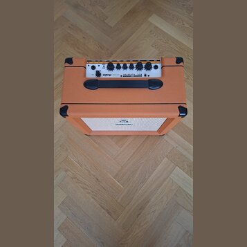 Kytarový kombozesilovač v oranžovém vinylu s černými plastovými rohy a úchytem. Na horním ovládacím panelu je bílý nápis ORANGE CRUSH 20 a řada ovlád…
