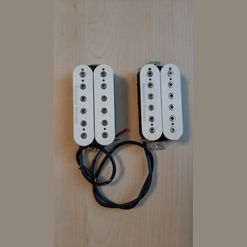 Dvě elektrické kytarové snímače typu humbucker s bílými plastovými kryty. Na obou je z levé strany svisle napsán nápis Seymour Duncan. Snímače mají č…