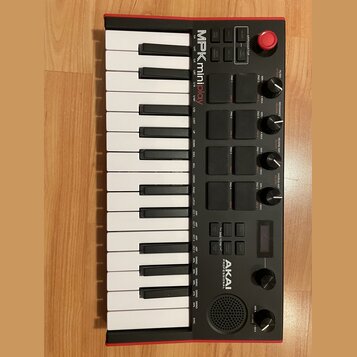Černý kompaktní MIDI kontrolér s červeným rámem. Na horní části je nápis MPK mini play a v dolní části logo AKAI PROFESSIONAL. Nástroj obsahuje kláve…