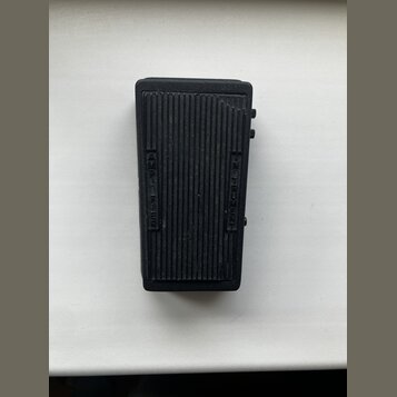 Černý obdélníkový efekt pedál z plastového nebo kovového materiálu s žebrovaným povrchem. Na levé straně je svisle vyražen nápis AMPLIFIER a na pravé…
