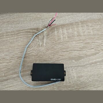 Černý elektrický snímač s obdélníkovým tvarem a dvěma montážními šrouby po stranách. Na spodní hraně je bílý nápis EMG-ESP. Ze snímače vede šedý kabe…