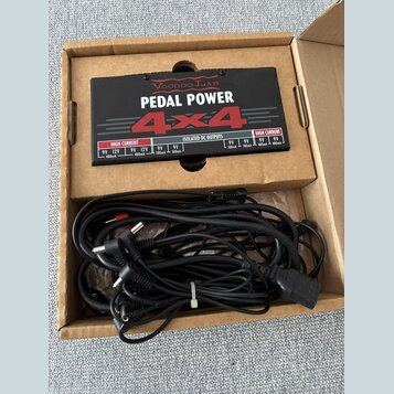 V kartonové krabici se nachází černý napájecí adaptér pro efekt pedály s nápisy VOODOO LAB, PEDAL POWER 4x4 a ISOLATED DC OUTPUTS. Na horní straně js…