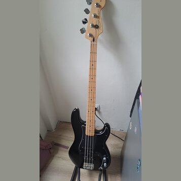 Černá elektrická basová kytara s hnedým javorovým hmatníkem a hlavou. Na hlavě je vidět logo Fender a nápis Precision Bass Special. Nástroj je umístě…