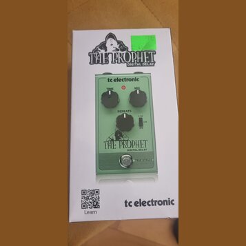 Fotografie znázorňuje krabici s efekt pedálem tc electronic THE PROPHET DIGITAL DELAY. Pedál je zelený, má tři černé ovládací knoflíky s popisky TIME…