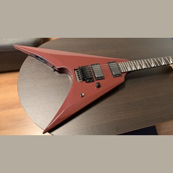Elektrokytara s červeným matným povrchem v ostrém, atypickém tvaru. Je vybavena dvěma černými humbuckery a černým tremolo mostem. Na těle se nachází…