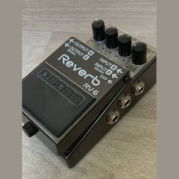 Kytarový efekt pedál v šedém kovovém provedení s černým spínacím pedálem. Na horní části je bílý nápis Reverb a model RV-6, v levé části je vyražené…