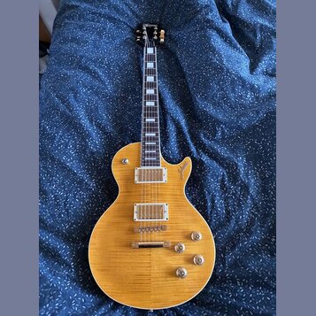 Elektrická kytara s žlutým průsvitným lakem a viditnou strukturou dřeva. Na těle je v oblasti horního výřezu nápis "Custom". Kytara má dva humbuckery…