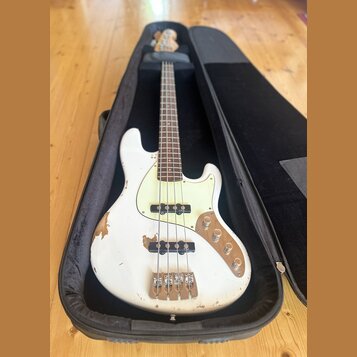 Bílá elektrická basová kytara v černém obalu. Nástroj má světlý hmatník, bílý pickguard a čtyři struny. Povrch bílého trupu vykazuje výrazné opotřebe…