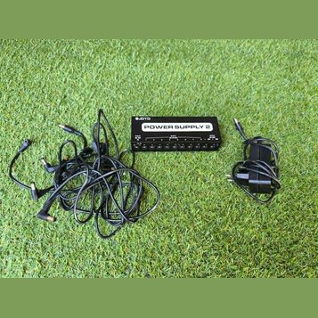 Černý napájecí zdroj pro efektové pedály s bílým nápisem POWER SUPPLY 2 a logem JOYO. Zařízení má v dolní části řadu výstupů pro konektory. K zdroji…