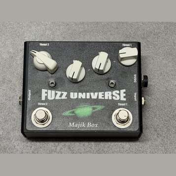Černý efekt pedál s nápisy FUZZ UNIVERSE a Majik Box. Na horní straně jsou čtyři bílé ovládací knoflíky s popisky Thrust 2 a Thrust 1. V dolní části…