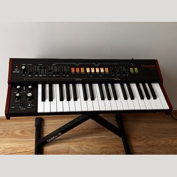 Červený vocoder značky behringer, model Vocoder VC340, s klaviaturní klávesou. Horní panel obsahuje řadu ovládacích knofíků, posuvníků a podsvícených…