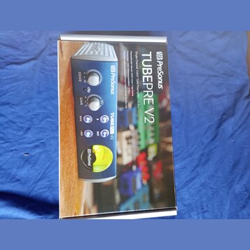 Fotografie znázorňuje krabici s produktem PreSonus TubePre V2. Na obalu je zobrazen modrý jednokanalový předzesilovač s ovládacími prvky Drive, Gain…