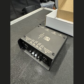 Černá stereo DI box s kovovým šasi a integrovaným stojánkem. Na horní straně je nápis „Palmer PAN 04 passive DI Box stereo“. Zařízení má dva vstupy o…
