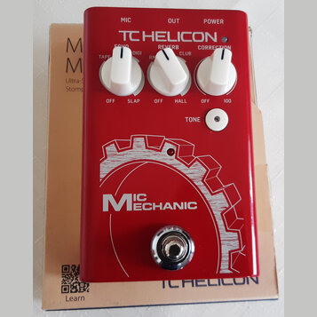 Červený efekt pedál s bílými nápisy a třemi bílými otočnými ovladači. Na horní části je logo TC HELICON a popisky MIC, OUT, POWER, ECHO, REVERB, CORR…