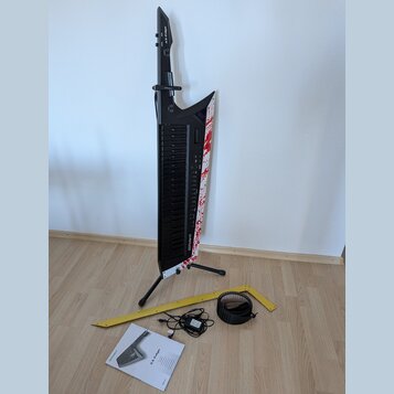 Černý keytar s bílým povrchem na pravém boku, který je zdoben červenými skvrnami připomínajícími krev. Na hmatníku je svisle napsáno AX-Edge a v doln…