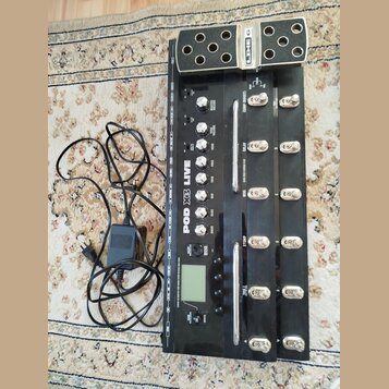 Černý kytarový procesor s kovovými spínači a ovládacími knoflíky. Na přístroji jsou nápisy LINE 6, POD X3 LIVE a označení sekcí jako COMP (BOOST), DE…