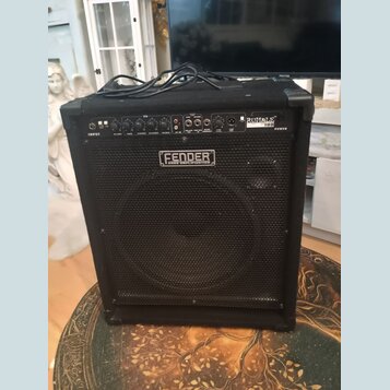 Černý basový kombozesilovač s mřížkou před reproduktorem. Na horním ovládacím panelu je nápis RUMBLE 100 a na přední mřížce logo FENDER BASS AMPLIFIC…
