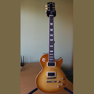 Elektrická kytara s trupem v žlutém gradientu (sunburst) a tmavým hmatníkem s trapezoidními vložkami. Na hlavě je bílý nápis Gibson. Nástroj má dva h…