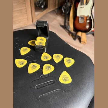 Žluté kytarové trsátka s černým potiskem loga „dunlop“ a nápisem „U.S.A.“. Na některých kusech je viditelný nápis „.73 mm“. Trsátka jsou rozprostřena…