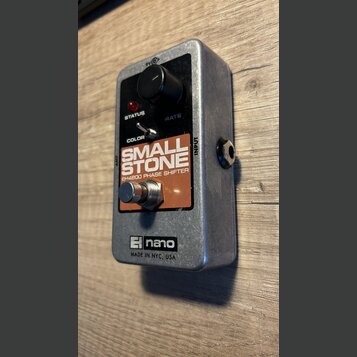 Stříbrný efekt pedál s černým ovládacím panelem a hnědým štítkem. Na štítku je bílý nápis SMALL STONE a pod ním EH4800 PHASE SHIFTER. Na spodní části…
