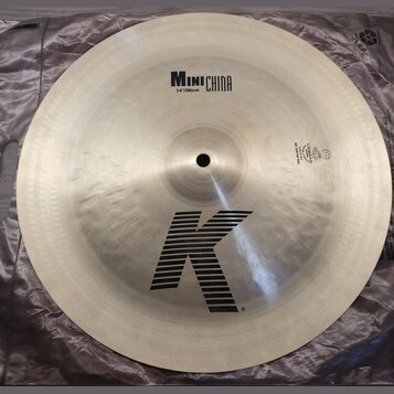 Kruhový činel z kovu s viditelným kování povrchu. Na horní části je nápis MINI CHINA a pod ním 14"/36cm, ve spodní části je velké logo K. V pravé čás…