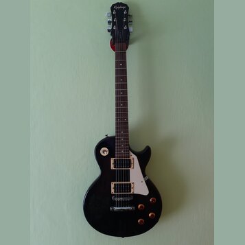 Černá elektrická kytara s tvarem single-cut a bílým pickguardem. Na hlavě hmatníku je bílé logo Epiphone. Nástroj má dva humbuckery s krémovými rámeč…