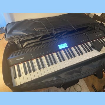 Černé digitální piano značky Roland, model GO:PIANO, umístěné v černé transportní tašce. Nástroj má bílé a černé klávesy a v horní části se nachází m…