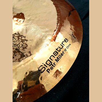 Detailní záběr na povrch mosazného činele s kovaným povrchem. Na čineli je černý nápis „Signature“ a pod ním menší text „Petr Milér 19" China“. Povrc…