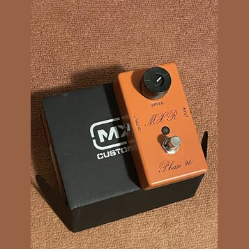 Oranžový efekt pedál s nápisy MXR, Phase 90 a SPEED. Na horní straně je černý ovládací knoflík a stoupací spínač. Pedál leží na černé krabici s bílým…