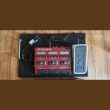 Červený multi-efektový procesor s nápisem ZOOM B3n Multi-Effects Processor. Zařízení má tři displeje, ovládací knoflíky a tři nožní spínače označené…