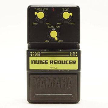 Černý kytarový pedál s nápisem NOISE REDUCER a označením modelu NR-100. Na horní části jsou tři žluté oválné ovladače s popisky THRESHOLD, DECAY a RE…